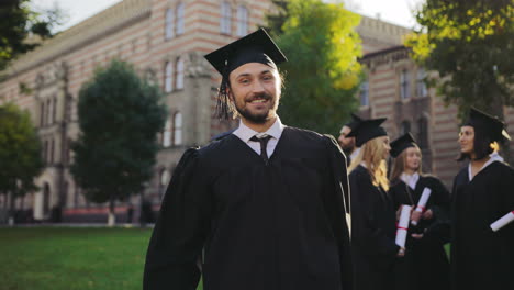 Portrait-shot-of-the-happy-cheerful-and-funny-man-in-traditional-graduation-gown-and-cap-with-diploma-in-hands-having-fun-and-grimacing-to-the-camera