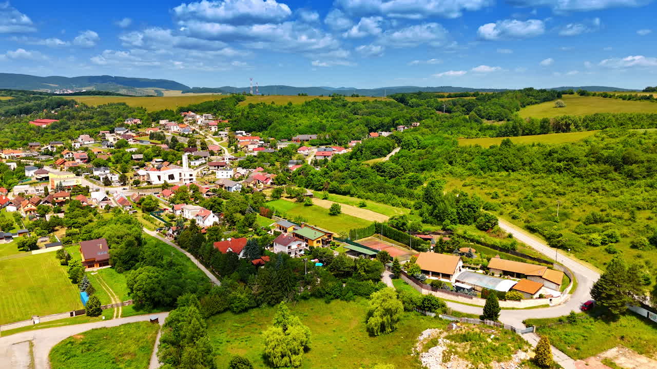 Scenic view of a quaint village. Lush greenery surrounds a picturesque village with scattered homes, clear skies, and rolling hills in the background