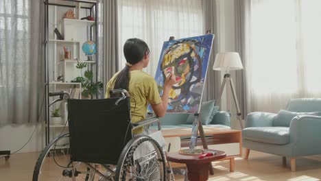 vista posterior de una artista asiática en silla de ruedas pensando y pintando el rostro de una niña en el lienzo