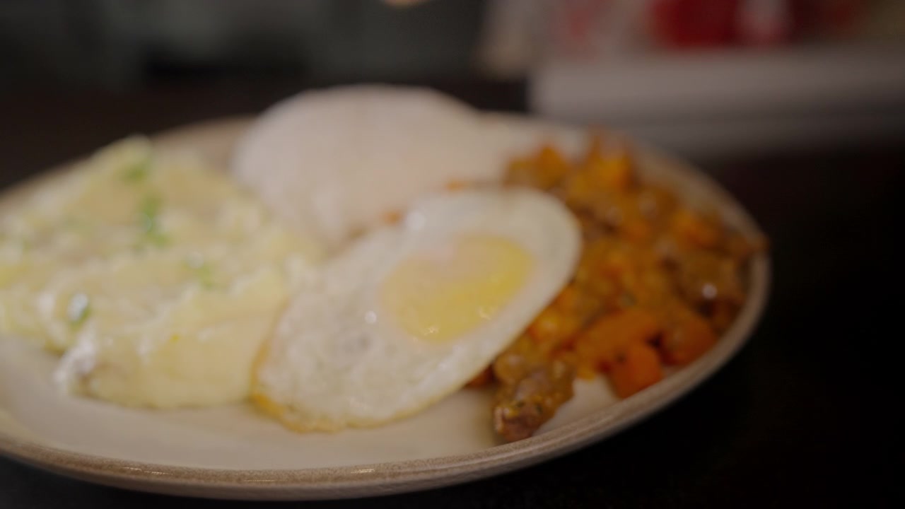 Toma con alejamiento de un plato emplatado con huevo frito y guarnición servidos en un plato en la cocina