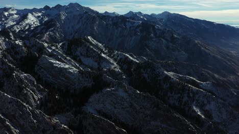 aerial view of mountain range on sunny winter day, snow covered peaks, tilt up drone shot