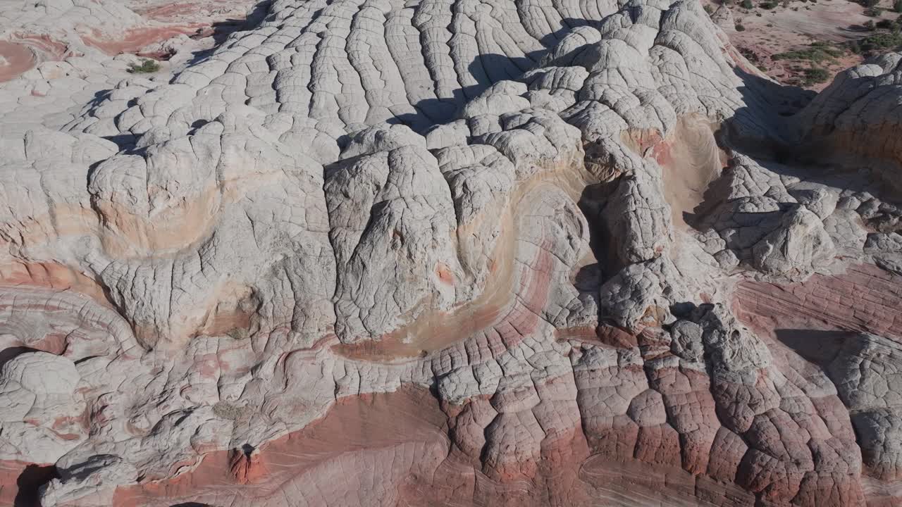 A drone flying forward and panning up to reveal the unique sandstone rock features of White Pocket Arizona surrounded by sandy desert and blue skies
