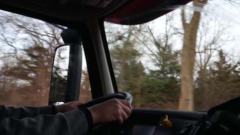 wide shot inside cabin semi truck, hands on steering wheel driving forward, shallow depth of field