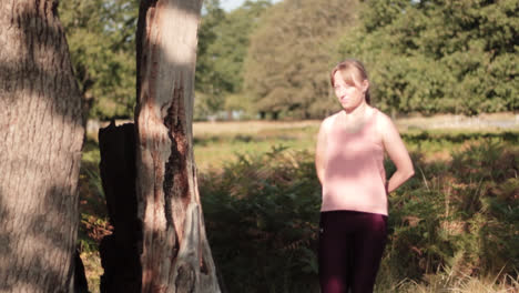 mujer estirando las piernas mientras está de pie junto al árbol para calentar sus articulaciones en el parque