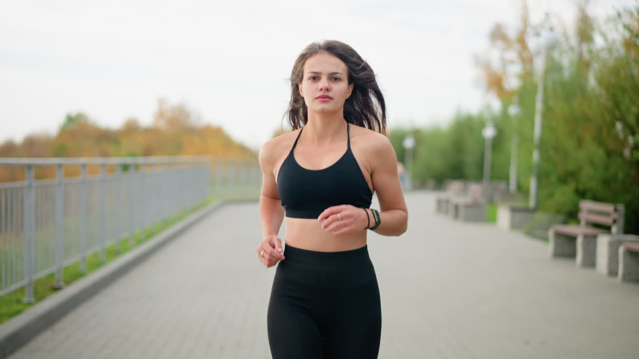 Close-up view of woman jogging in black fitness wear in park with benches and trees in background, active lifestyle, fitness, and healthy running in outdoor park setting