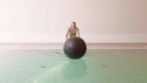 woman jumps and successfully grabs on to floating exercise ball in pool