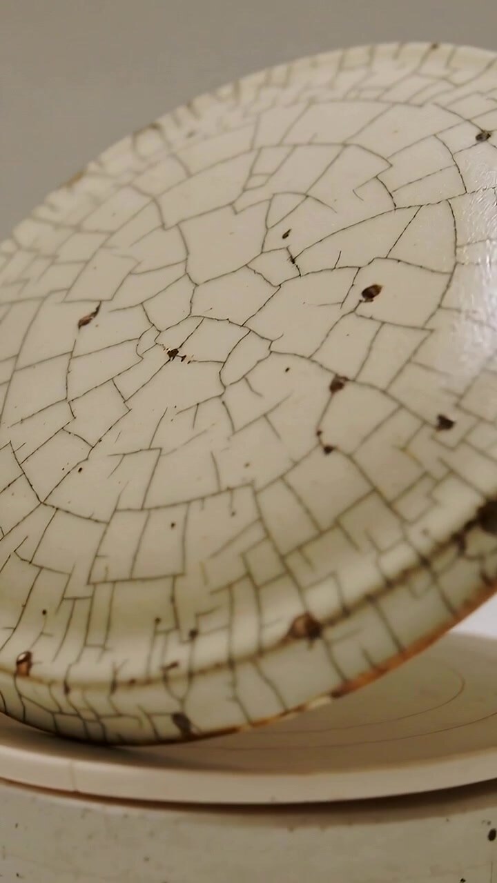 Vertical video: Tilting crackled brown-specked lid on pale table revealing rim wear and base shadow