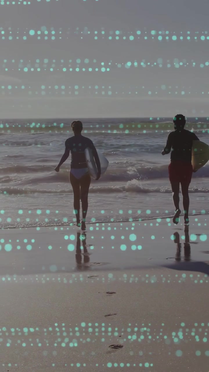 Vertical video: Waves urging couple running into surf to ride waves, carrying boards, teal overlay