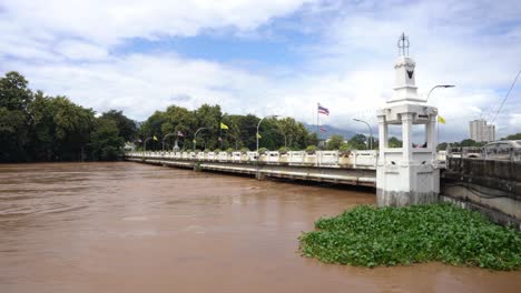 wide shot of nawarat bridge in chiang mai thailan mae ping river floods and reaches bridge level fast-flowing brown water with electric cables submerged,thai flags on bridge flooding, september 2024
