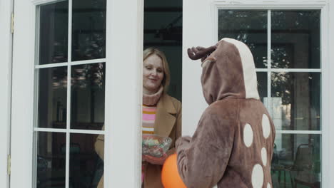 the child comes to get candy at the door of the house. woman opens the door and gives a treat