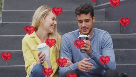 Animation-of-heart-icons-floating-over-happy-caucasian-couple-talking-and-drinking-takeaway-coffee