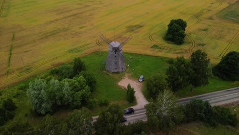 aerial shot of an old windmill in the field by the road, zooming out