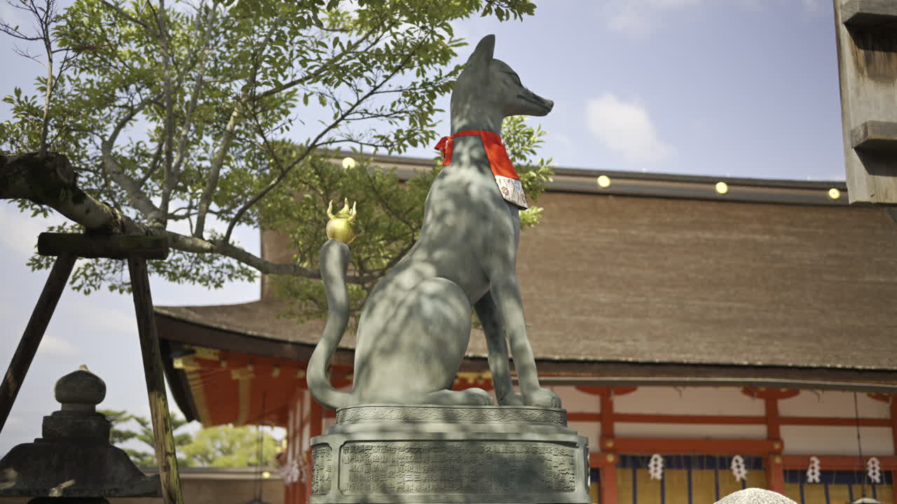 A graceful fox statue stands proudly at Fushimi Inari traditional Japanese shrine, decorated with a vibrant red scarf
