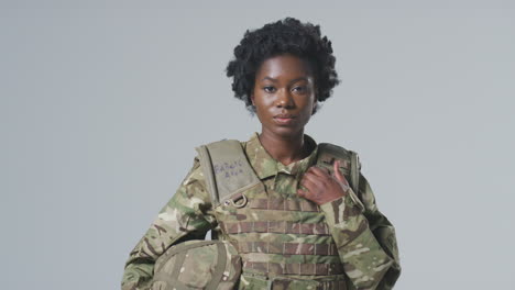 studio portrait of serious young female soldier in military uniform against plain background