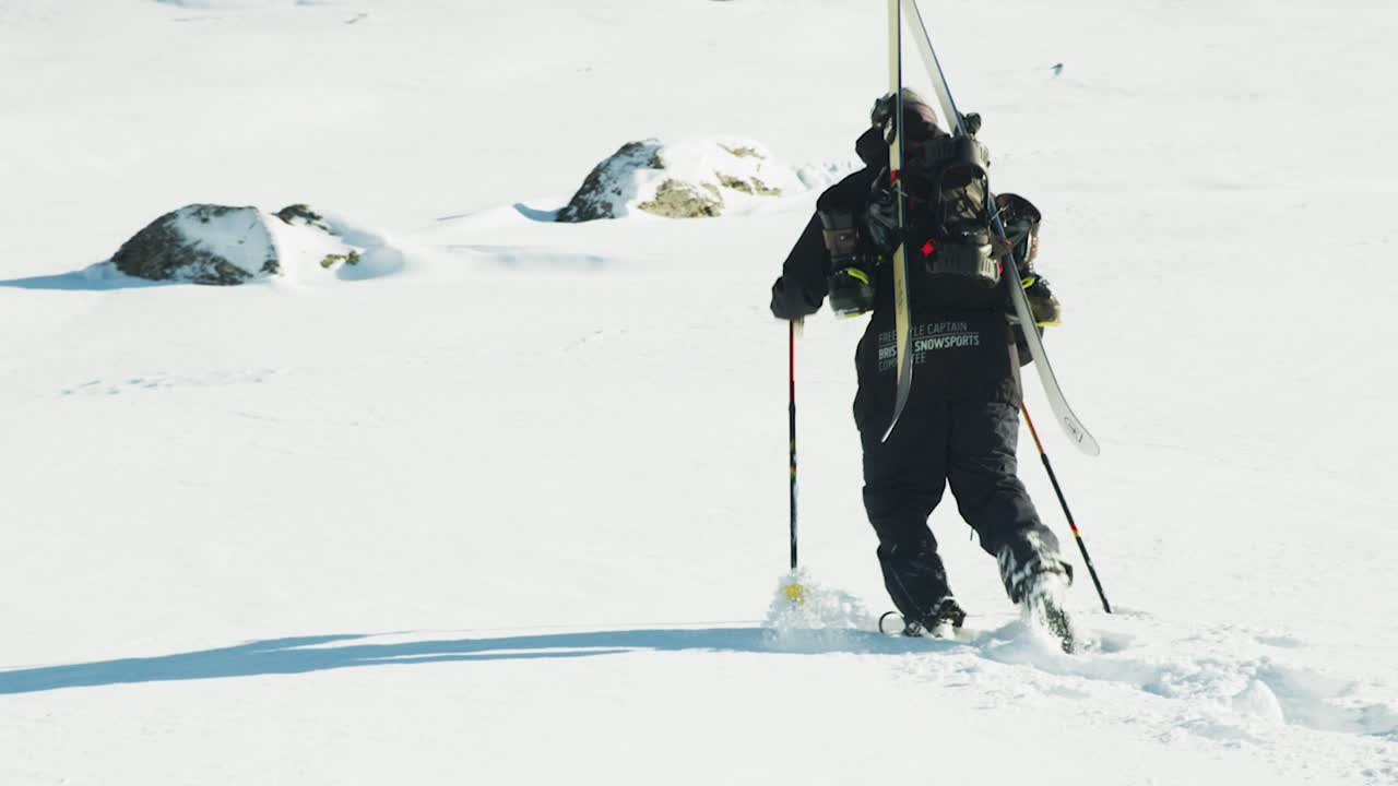 hombre caminando con esquís en la espalda a través de la nieve profunda en un soleado día en las montañas francesas