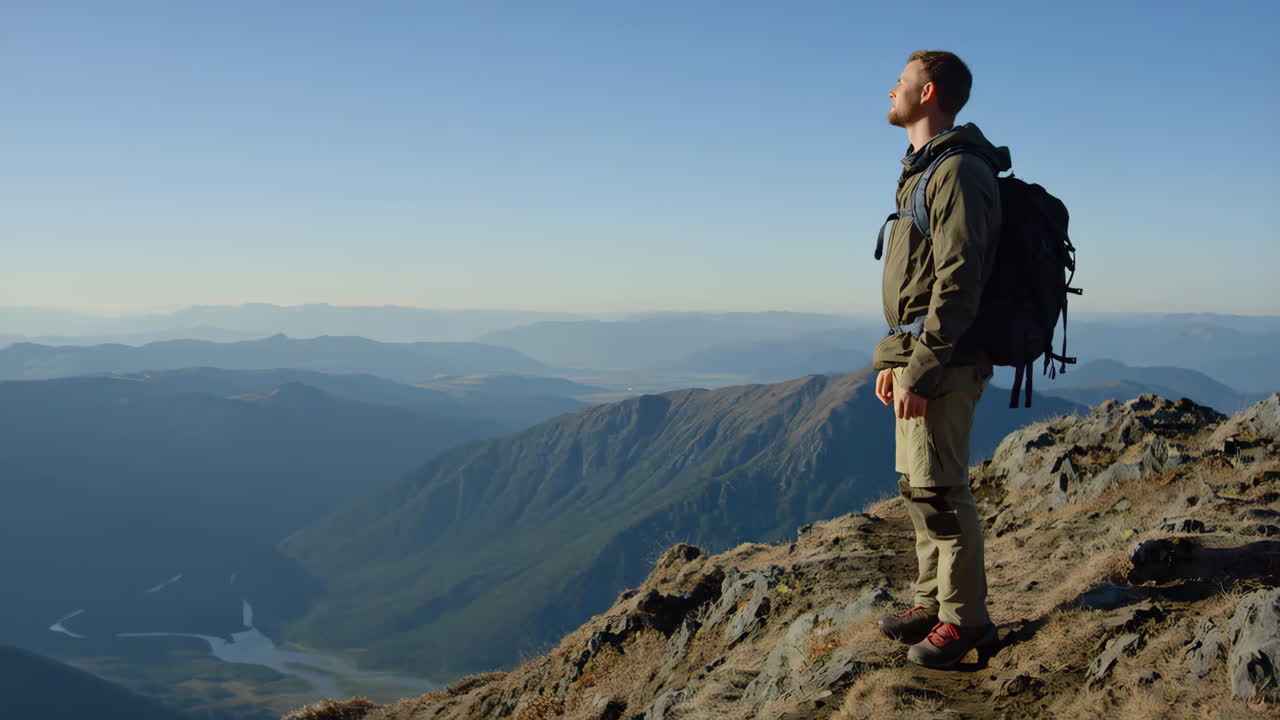 Man with backpack standing on a mountain peak overlooking a vast landscape