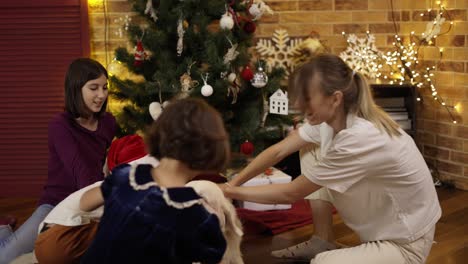 three kids and mom stroking and tickling golden retriever dog on the floor under decorated new year tree