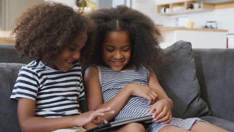 Brother-And-Sister-Sitting-On-Sofa-At-Home-Playing-With-Digital-Tablet