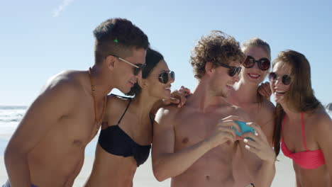 mixed race group of friends taking selfies on the beach using phone camera