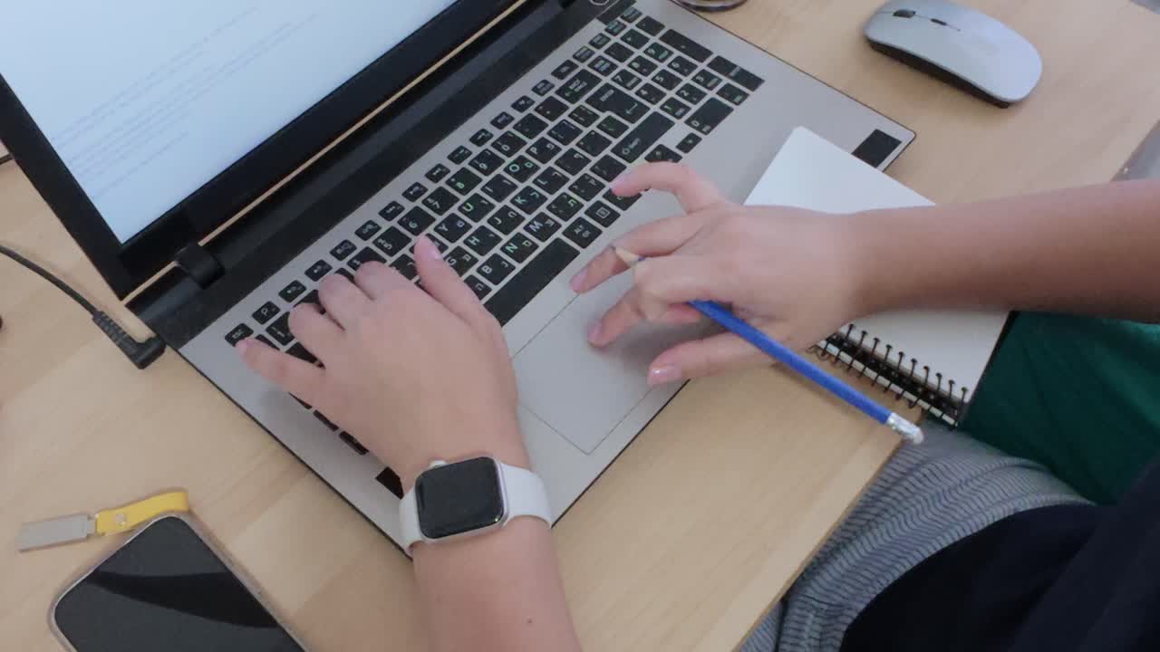 Hands organizing thoughts and plans, writing in a notebook alongside a laptop.