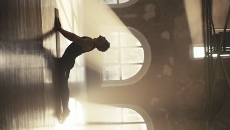 vertical video of a male athlete in a black sports summer uniform doing stretching exercises and strengthening the muscles of the back in the sunny hall