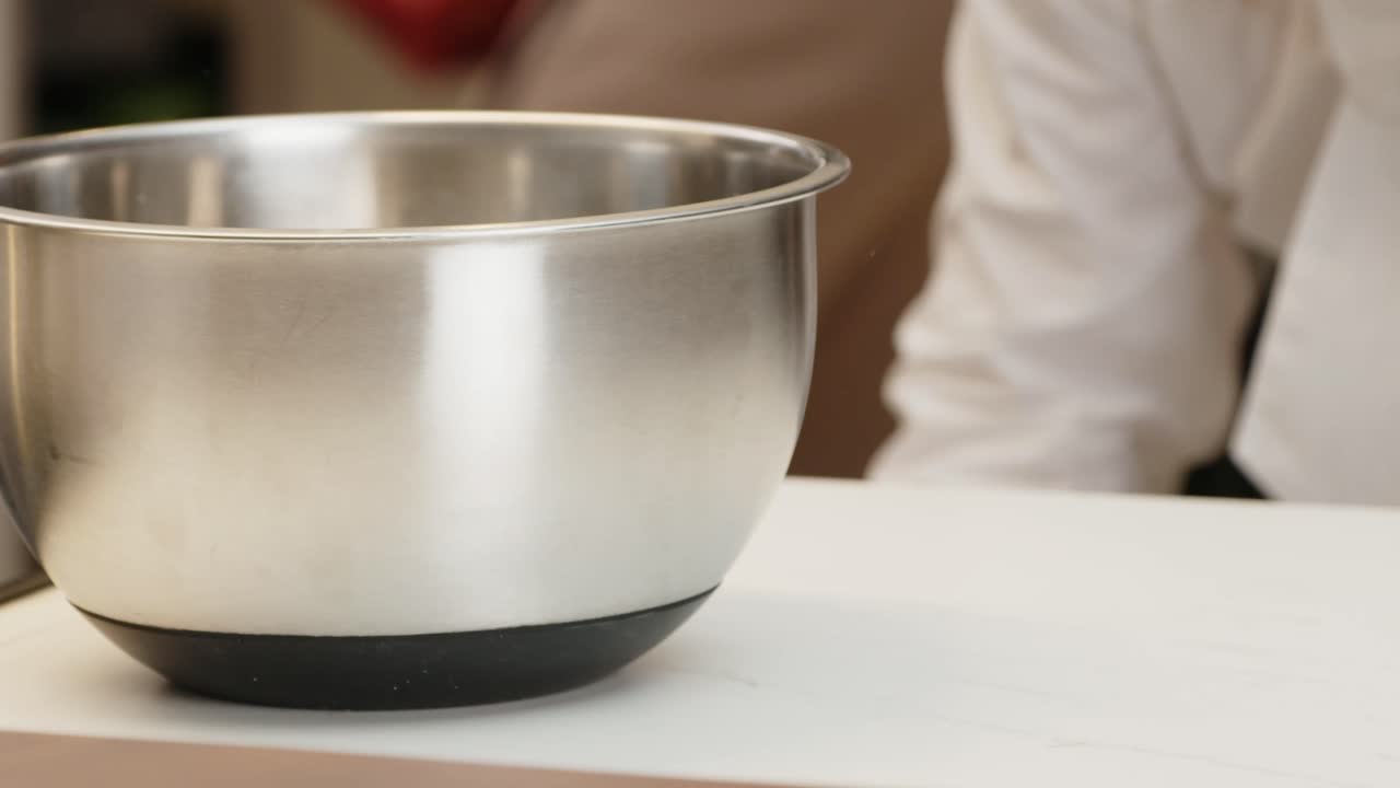 Shiny stainless steel mixing bowl on a white table in a kitchen