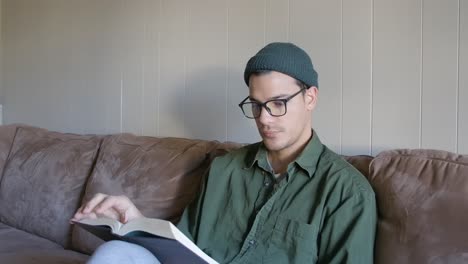 Young-Man-at-Home-Reading-a-Book-in-the-Couch-STATIC