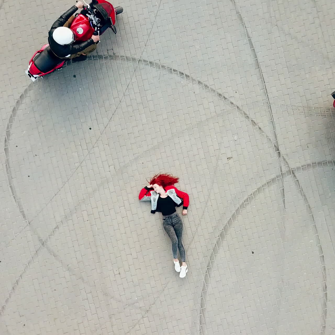 Close-up of an extreme red-haired woman is lying on the road outdoors. Beautiful young female and three motorbikers riding around her. Aerial view. Camera moves up around in a circle.