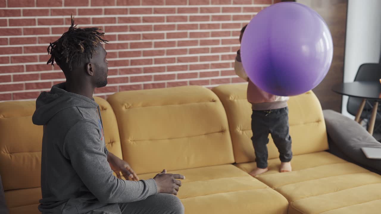 padre afroamericano jugando con un niño lindo en el sofá en el interior acogedor de la casa
