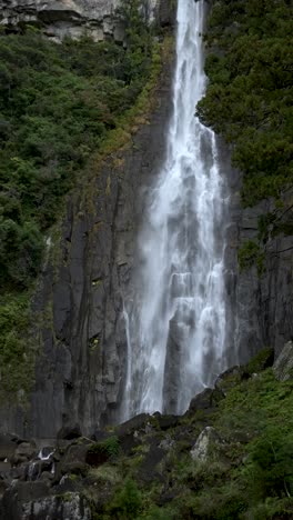 a grand waterfall flows down rocky cliffs surrounded by lush greenery and trees. vertical video
