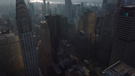 High-angle-view-of-buildings-in-midtown.-Tilt-up-reveal-of-majestic-office-tower.-Hazy-view-of-Empire-State-Building-against-sun.-Manhattan,-New-York-City,-USA