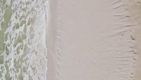 Aerial-vertical-abstract-showing-sand-beach-and-emerald-waves-rolling-onto-the-sand