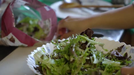 hand placing salad lettuce from packet onto plate in kitchen