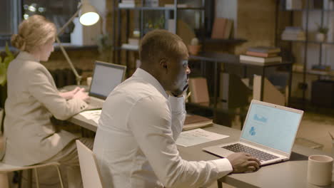 side view of american man observing stadistics and graphics on computer monitor sitting at desk in the office