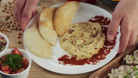 israeli cuisine. putting plate with hummus decorated with paprika and pita close-up. national food, middle eastern culture. vegan chickpea puree snack. appetizer made from mashed chickpeas