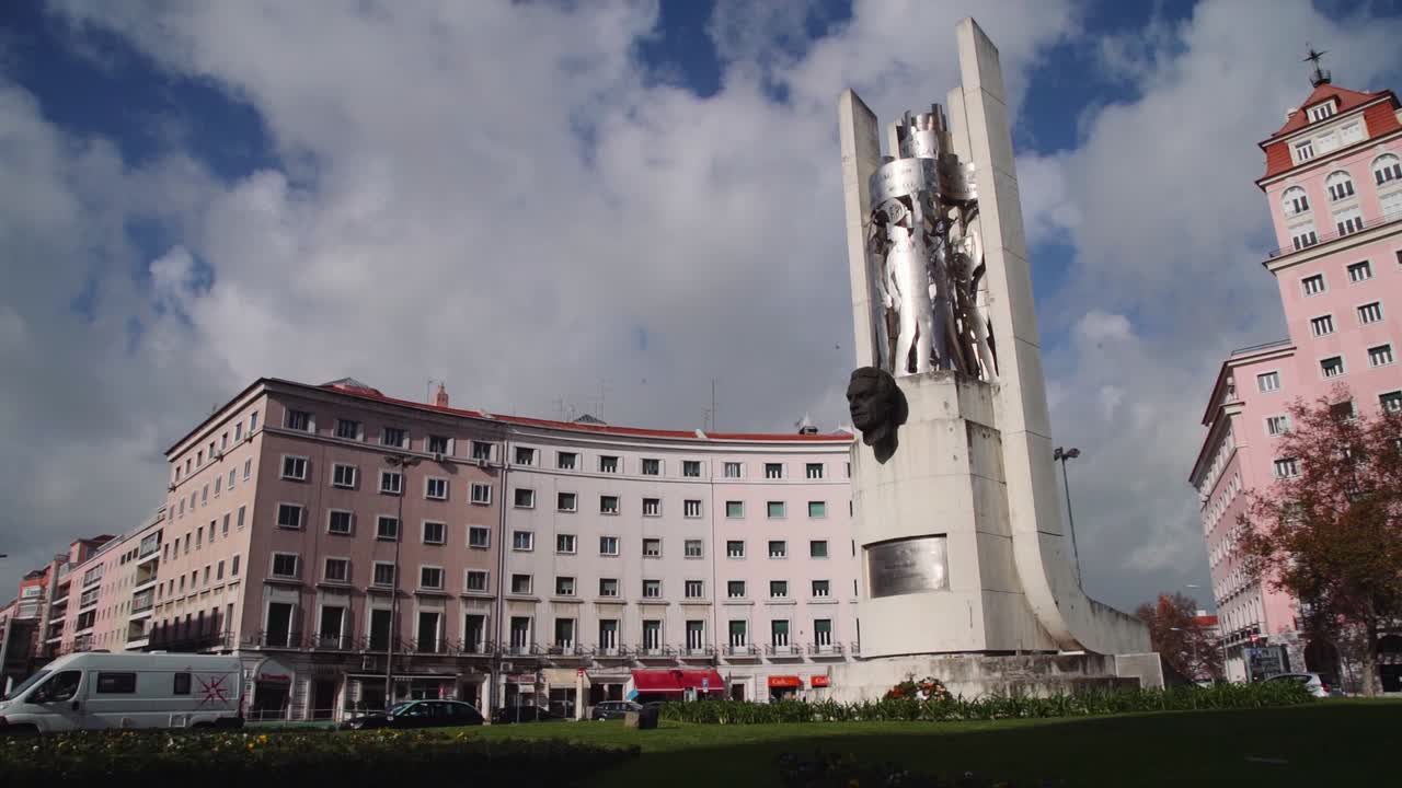 estatua circular en cámara lenta en una rotonda con coches y edificio en segundo plano.