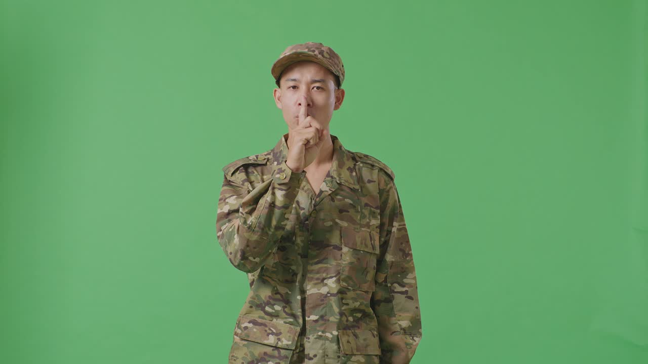 Asian Man Soldier Looking At Camera And Making Shh Gesture While Standing In The Green Screen Background Studio