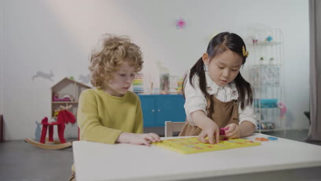 little girl and little boy playing with alphabet puzzle in montessori school while other pupils running in the classroom