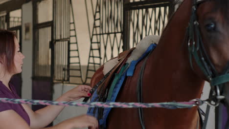 mujer preparando un caballo para montarlo en un establo