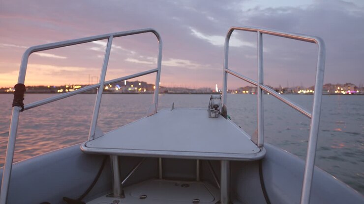 POV cinematografico dalla parte anteriore di una barca all'alba ad Agde, in Francia, con le luci della città che si riflettono sulle acque calme sotto un cielo mattutino colorato