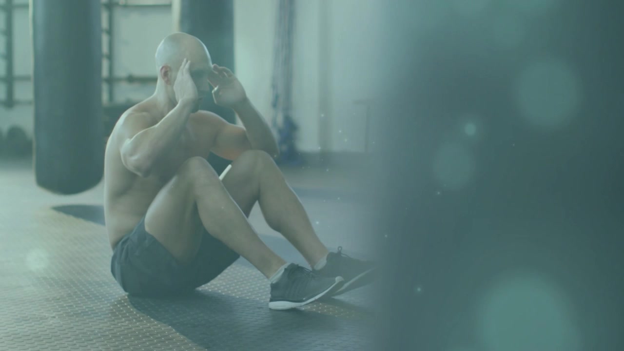Uomo che esegue sit-up sul pavimento della palestra, bokeh color verde acqua che si dissolve e rivela attrezzature per il fitness