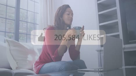 Animation-of-speech-bubble-with-thumbs-up-likes-and-numbers-over-woman-having-tea,-using-laptop