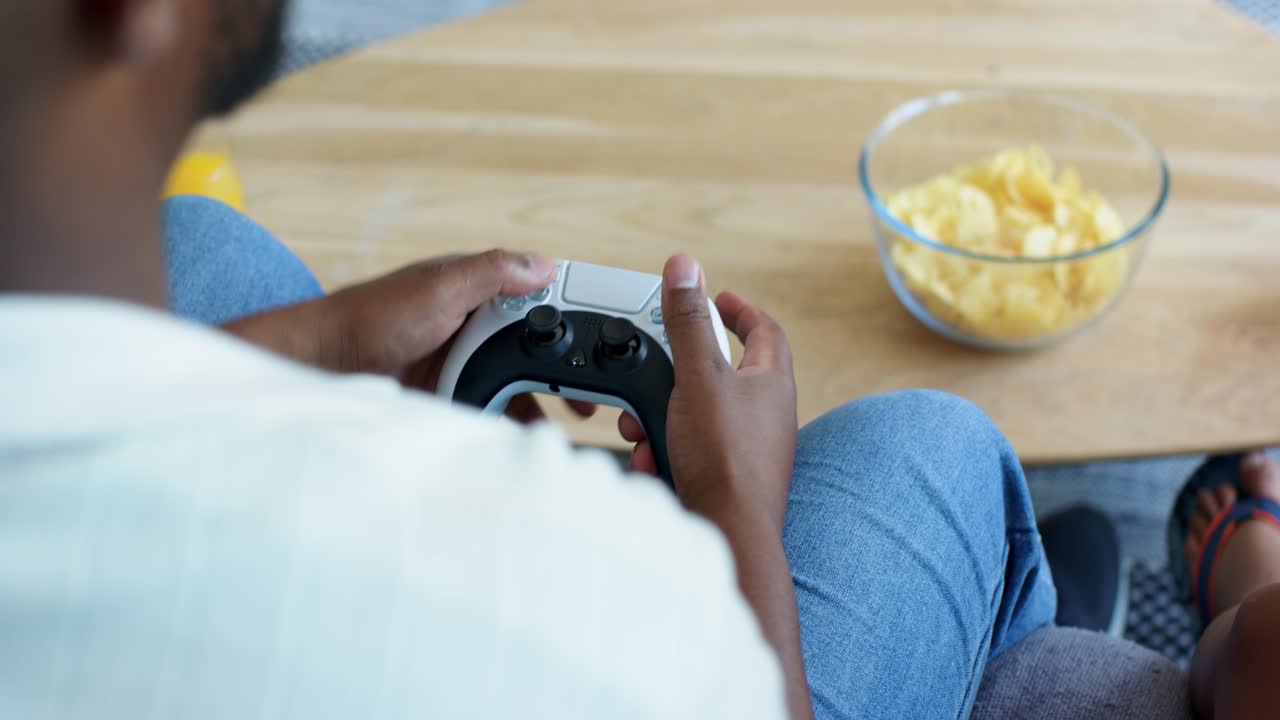 Man is adjusting grip on controller, seated on sofa near coffee table with chips, for gaming