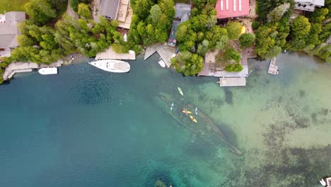 Toma-Aérea-De-Arriba-Hacia-Abajo-De-Kayakistas-Uniéndose-En-La-Cima-De-Un-Naufragio-En-El-Puerto-De-Big-Tub,-Península-De-Bruce,-Bahía-Georgiana