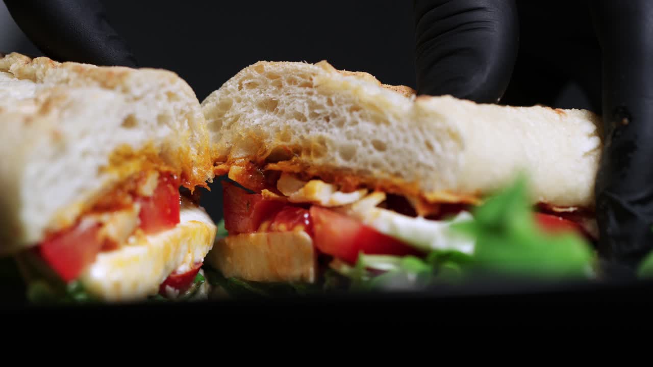 Un panino diviso a metà con carne, pomodori e insalata è aperto.