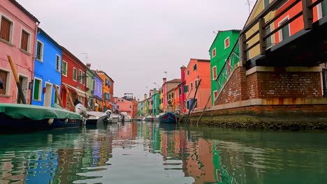 water surface pov view of burano picturesque colored houses and canal with moored boats, italy