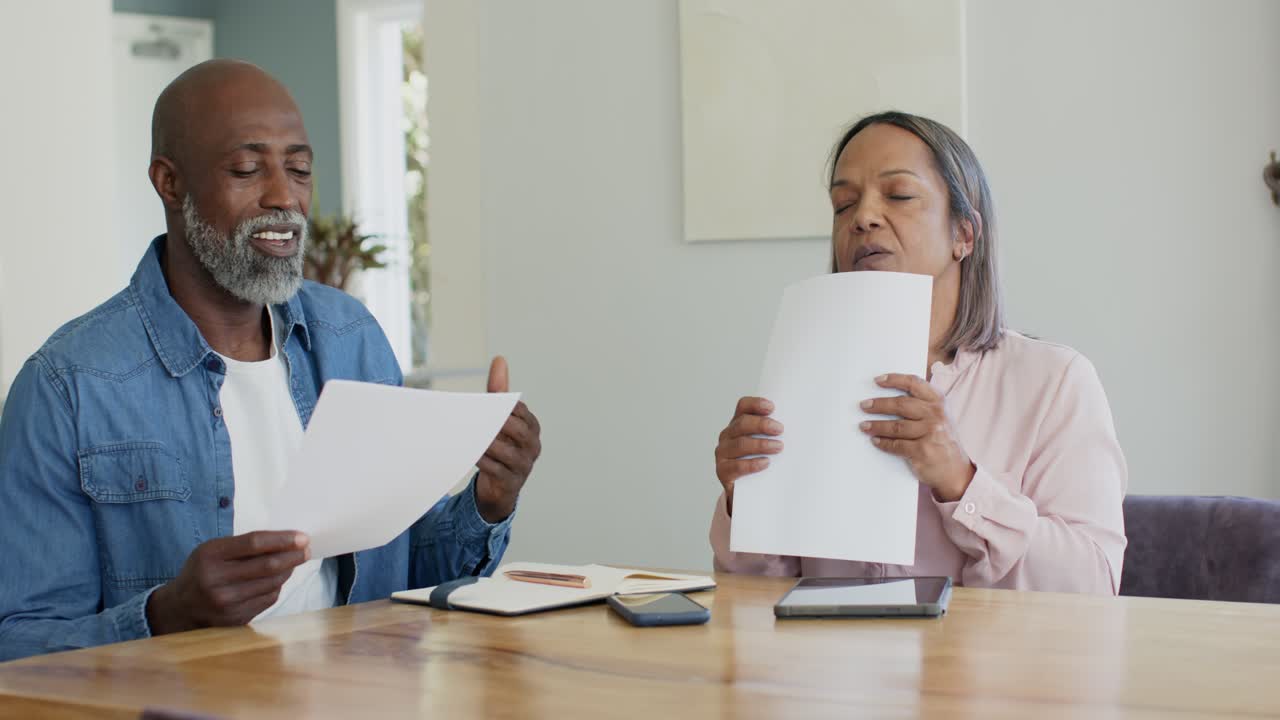 Couple, African American man showing sheet and woman scanning stack at wooden table, sorting bills