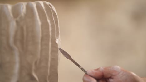 man carefully and attentively designing clay pot using professional pottery tools. inspired potter creating unique ceramics product. close-up, blurred background