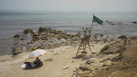 life guard sits on duty on the beach near cala de mijas on the costa del sol in southern spain while a holiday makers sits beneath parasol.