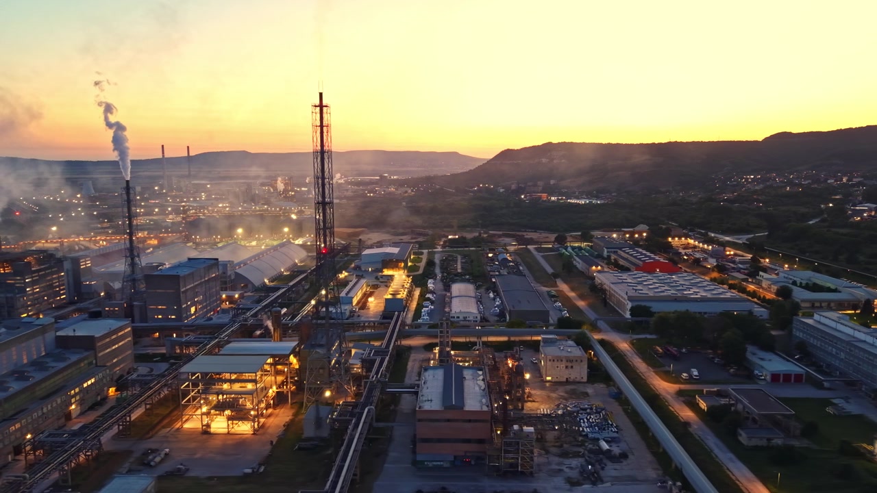 Area industriale vista al tramonto con fabbriche, ciminiere e attrezzature attivamente in funzione vicino a colline